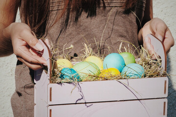Closeup of female person hold wooden basket full of multi colored painted easter eggs at white background. Easter holiday concept