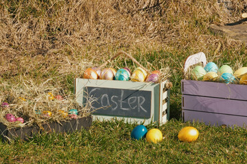 multi colored painted easter eggs in wooden planter on the green grass. Easter holiday concept