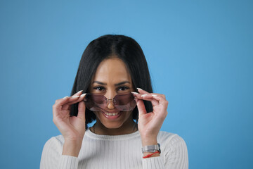 Portrait of beautiful toothy smiling African american woman with trendy sunglasses looking at camera, cutout on blue background