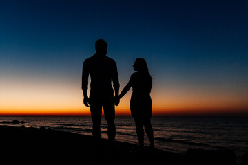 Loving couple in white clothes during a honeymoon at sea walk on the sand at a photoshoot Love Story, ocean coast, beach, silhouette