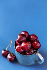 Fresh cherries in a metal mug on a light blue background.