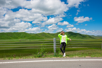 Fototapeta premium A woman in the blue sky and white clouds of the grassland road side.