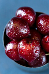 Fresh cherries in a metal mug on a light blue background. Macro food photo.