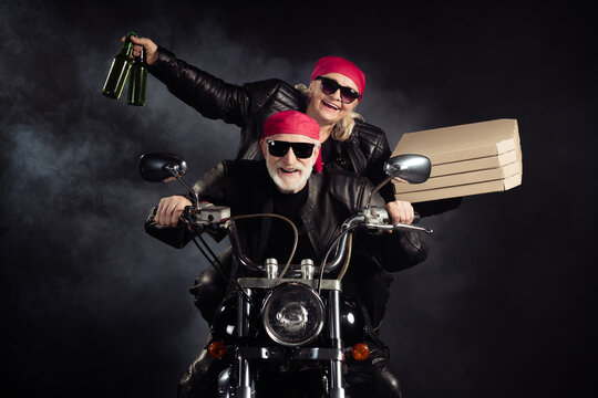 Photo of cool old bikers white hair man lady couple drive chopper moto travel pensioners party bring takeaway pizza beer bottles wear rocker leather outfit isolated black color background