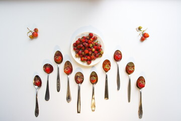 Alpine strawberry (wild strawberry) on a white background. Top view.
Strawberries in teaspoons and in a saucer and two branches with berries on the edges.