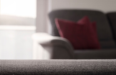 Fläche aus grauem Stoff im Vordergrund als Retusche-Vorlage, Wohnzimmer mit grauem Sofa, rotem...