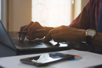 Casual business man hands typing on laptop computer keyboard with business graph diagram  data paperwork ,mobile phone and cup of coffee on the desk at modern home office. Digital marketing concept.