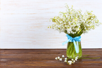 bouquet of lilies of the valley in a vase with blue ribbon on a brown white wooden background