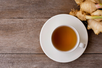 Obraz na płótnie Canvas Fresh organic young ginger roo and white cup of hot ginger tea isolated on wood table background . Natural herbal healthy drinks concept.