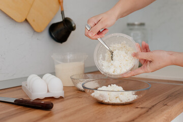 Cheese pancakes. The process of making cheesecakes in the home kitchen. A bowl of cottage cheese, a woman pours the cottage cheese into a bowl and drives an egg. Cottage cheese and yolk.
