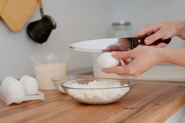 Cheese pancakes. The process of making cheesecakes in the home kitchen. A bowl of cottage cheese, a woman pours the cottage cheese into a bowl and drives an egg. Cottage cheese and yolk.