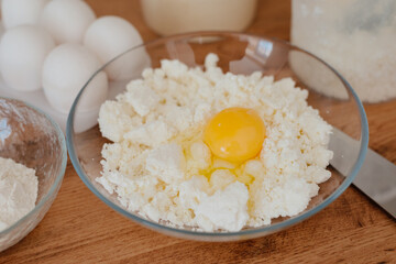 Cheese pancakes. The process of making cheesecakes in the home kitchen. A bowl of cottage cheese, a woman pours the cottage cheese into a bowl and drives an egg. Cottage cheese and yolk.