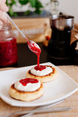 Healthy breakfast. Cheesecakes on a white plate. Breakfast in the home kitchen. Cheesecakes on a plate, next to a jar with sour cream and raspberry jam. Sour cream and raspberry jam.