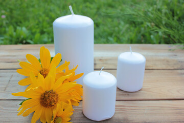 Fototapeta na wymiar White candles and yellow flower on the wooden table in the summer garden