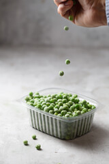 Mans hand holds peas in the storage box on the kitchen table, vertical orientation