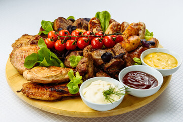 plate with fried meat, a wooden plate on a white tablecloth with fried meat, steak, barbecue, tomatoes and sauce