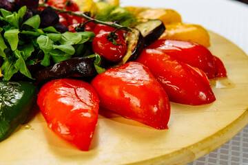 plate with boiled vegetables, a wooden plate on a white tablecloth with red green and yellow peppers and tomatoes