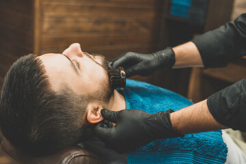 Haircut head and beard in a barbershop. Barber puts on and combs client’s beard. Process of creating a hairstyle and styling a beard for men. Man in a barbershop. Equipment stylist. Selective focus