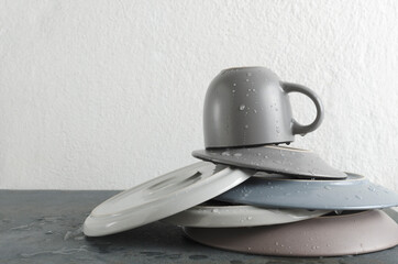 Closeup of stack clean and wet plates, cup on the grey table against white wall.Empty space