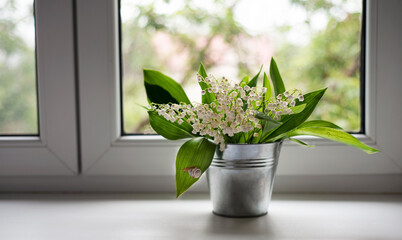A bunch of lily of the valley flowers in a bucket on window sill