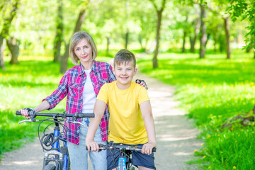 Fototapeta na wymiar Portrait of a happy sporty family holding bikes in a summer park. Smiling woman hugs her young son. Empty space for text