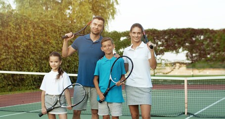 Portrait of happy family standing on court with racket in hands.
