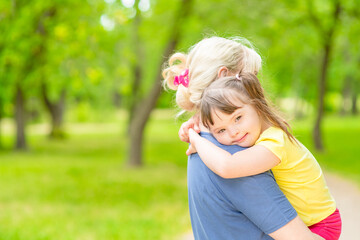 Happy little girl with syndrom down hugs mother in a sunny summer park. Empty space for text