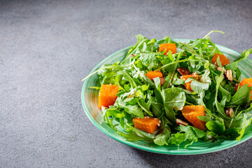 Delicious salad with arugula, baked pumpkin, hazelnut and sesame seeds on green plate. Paleo diet food concept.