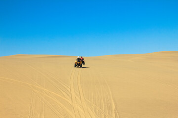 Fototapeta na wymiar Quad driving people - two happy bikers in sand desert dunes, Africa, Namibia, Namib, Walvis Bay, Swakopmund.