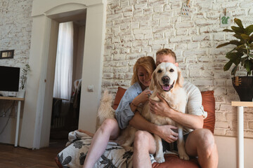 couple with dog sitting on a couch in their modern flat and having fun.  retriever looking straight to the camera