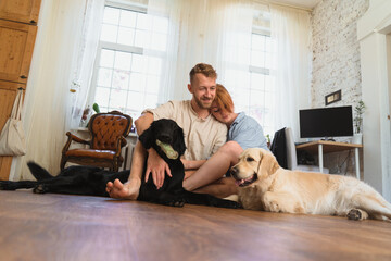 young couple with dogs sitting on the floor of their flat and having fun. dogs playing with their toys. man and woman hug each other and spend leisure  time with their dogs