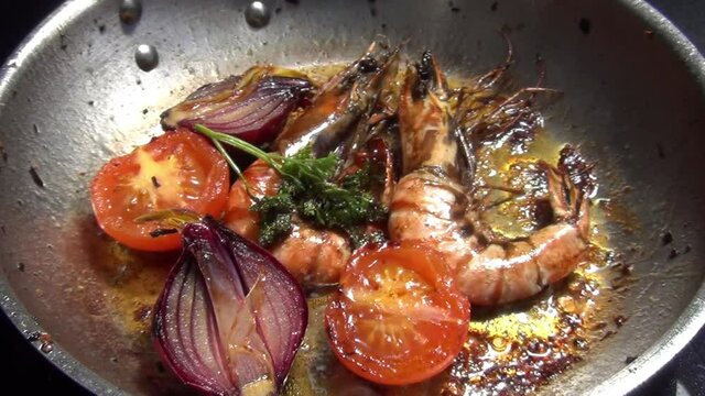 Hairy caucasian white male hand adjusts tiger prawns and vegetables which are cooking in melted garlic butter in a stainless-steel pan