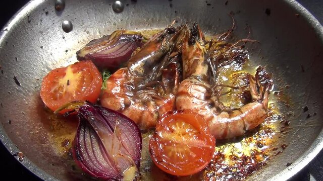Caucasian white male hand adjusts tiger prawns which are cooking in melted garlic butter in a stainless-steel pan