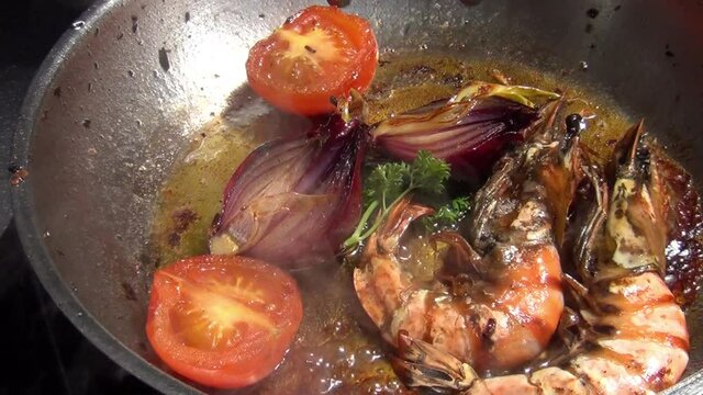 A zoom out footage of two tiger prawns, red onions, tomatoes and curly parsley sizzling in melted garlic butter in a stainless-steel pan
