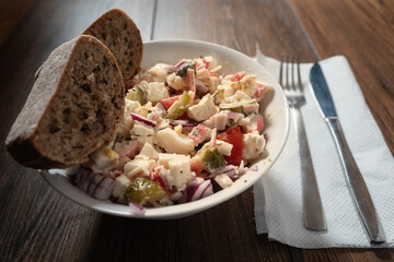 Fresh crab stick salad with brown bread in a white plate on wooden table. Fork and knife on a white serviette. Selective focus.