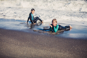 Fototapeta na wymiar Two friends kids enjoying a funny surf day in the shore of a sunny beach in their coastal holidays 