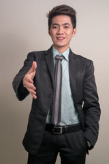 Fototapeta premium Portrait of happy young Asian businessman in suit giving handshake