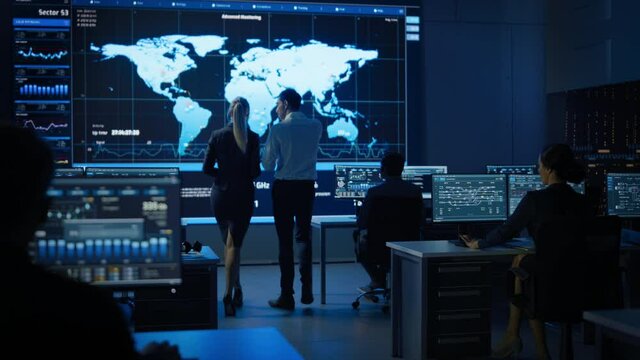 Project Manager and Chief Engineer Discuss Data Shown on Big Display. Screens Show Infographics, Charts, Information Analysis and Global World Map Data.Telecommunications Control Control Room 