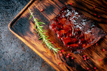 Grilled pork ribs with barbecue sauce on a wooden Board with spices and rosemary on stone background