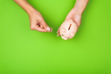 female hands put money in a piggy bank on a green background. Savings concept.