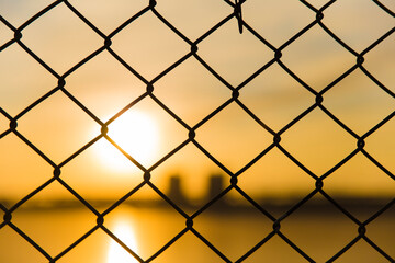 Fototapeta premium watching sunset Cityscape through mesh fence , blur