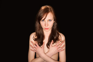 Obraz premium Classic nude of an attractive young woman hiding her breasts with her hands in front of black studio background