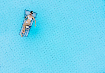 Aerial top view of slim young woman in bikini on the air mattress in the big swimming pool.