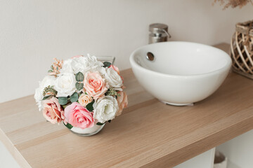 Artificial flowers in the bathroom interior. Decorative flowers in a round vase. Artificial flowers in a round vase. White bathroom interior. Decorative flowers. 