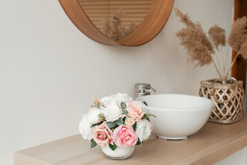 Artificial flowers in the bathroom interior. Decorative flowers in a round vase. Artificial flowers in a round vase. White bathroom interior. Decorative flowers. 