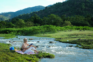 Happy time of tourist sitting on near the river and reading the book. Relex concept for green season.