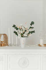 Artificial flowers in the interior. Decorative flowers in the interior. Artificial flowers in a vase. White interior of the room. Decorative fireplace. 
