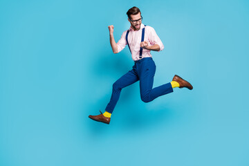 Fototapeta na wymiar Full size profile photo of handsome man jump high up running competition raise fists first place winner race marathon wear specs shirt suspenders pants boots isolated blue color background