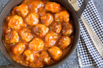 Meatballs in sweet and sour tomato sauce with spices served in a frying pan on dark background .