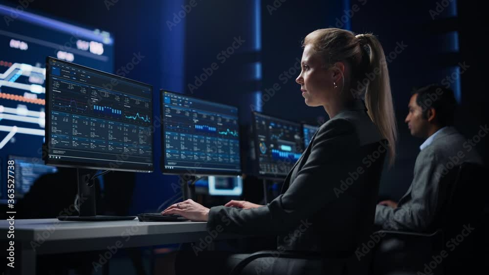 Poster confident female data scientist works on personal computer in big infrastructure control room. stock